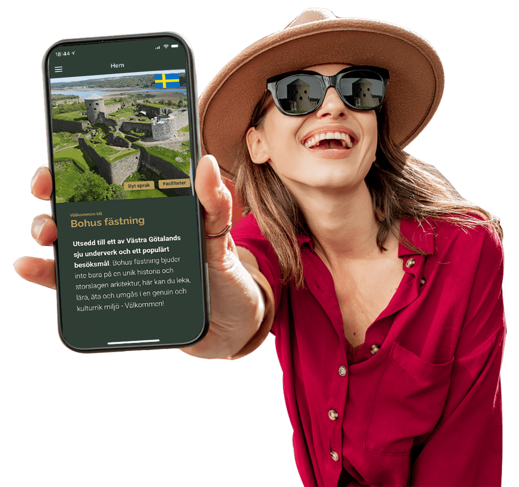 happy woman in hat and sunglasses shows off her mobile display of bohus fortress website