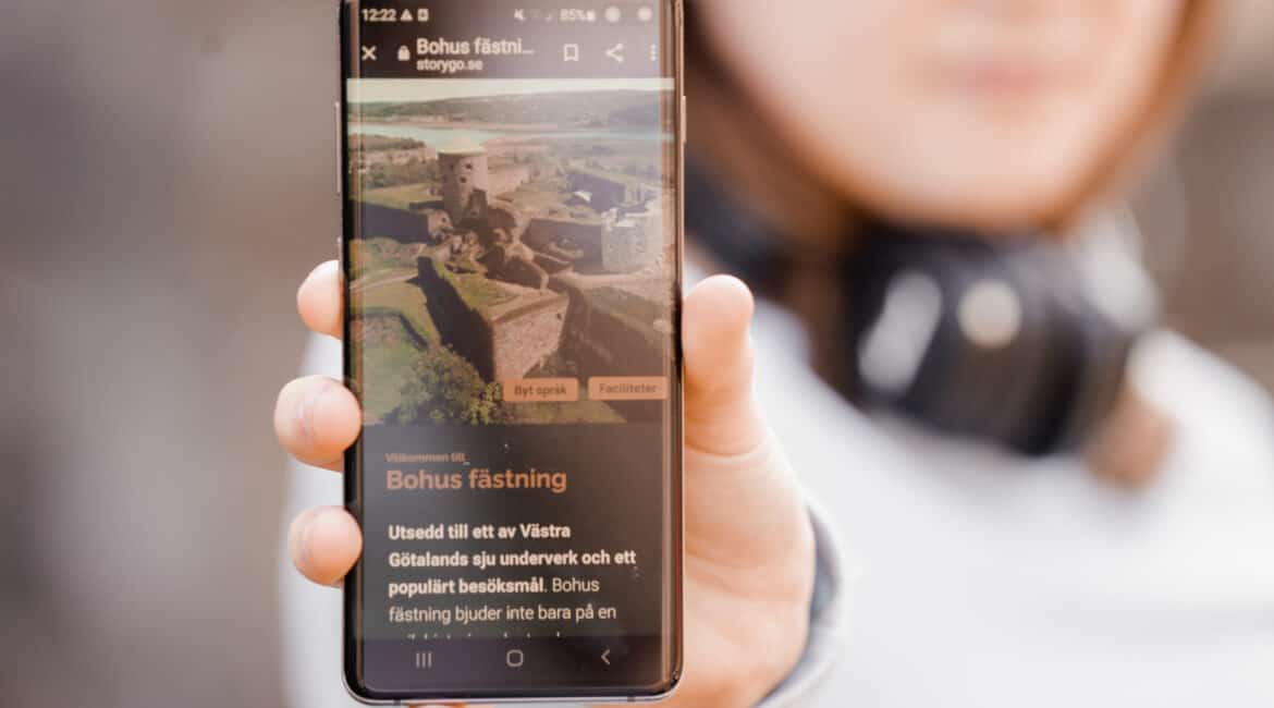 kvinna håller upp mobildisplay av besöksmål bohus fästnings nya digitala guidning